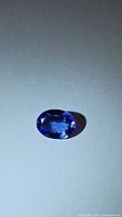 Close-up photo of a single oval cut tanzanite gemstone with deep blue color on a light background.