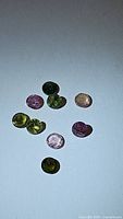 Photo showing nine small round cut multicolored tourmaline gemstones in green, pink, and yellow colors with visible inclusions.