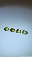 Four pear teardrop cut natural peridot gemstones laid in a row showing color, shape and cut details.