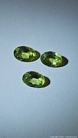 Three oval cut Peridot gemstones shown from an angled top view on a white background.