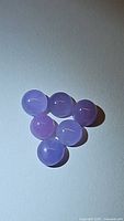 Six natural round cabochon purple chalcedony gemstones arranged in two rows, all stones showing from the top, displaying smooth rounded surfaces and purple translucent color.