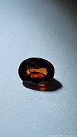 Close up photo of a single oval cut orange spessartite garnet gemstone showing color and facets.