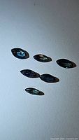 Six marquis cut blue-green natural sapphires laid out on a white surface. Stones show varying internal reflections and clarity.