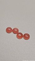 Four round, polished strawberry quartz cabochons lying on a grey fabric background, showing consistent reddish-pink color and smooth dome shapes.