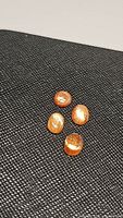Photo showing four natural sunstone gemstones placed on a textured dark surface. The stones are oval cabochon cut with visible flashes of light.