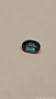 Oval natural topaz gemstone lying on a beige background showcasing aqua blue-green color and clear faceted cut.