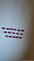 Photo showing eighteen marquis cut natural rubies arranged on a flat light surface, demonstrating size and color.