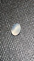 Natural white moonstone oval cabochon gemstone on textured dark gray fabric showing its translucent and adularescent qualities.