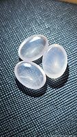 Three translucent oval cabochon rose quartz stones arranged on a dark textured surface showing their soft pink color and polish.