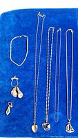 Overall shot on blue cloth showing 4 necklaces, 4 pendants, bracelet and single earring