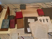 Multiple antique hardcover school books, loose paper sheets including drafting images, and music instruction booklets on a fabric surface.