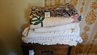 Stack of four folded vintage bed covers including patterned quilt and textile pieces on a wooden surface