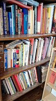 Three wooden shelves filled with books of various sizes and topics, mostly non-fiction.