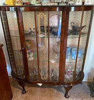 Front view showing full cabinet with curved glass doors and shelves inside, glassware displayed inside.