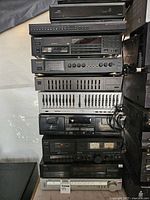Stacked view of 11 various electronic stereo and video components including cassette decks, equalizers, mixers, tuners, DVD player