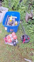 Blue plastic storage bin containing assorted fishing reels, a tackle box, and various fishing accessories. Next to the bin are three orange fishing buoys and a black and red reel spool.