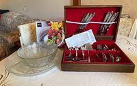 Partial flatware set in wooden box with red lining, glass bowls and glass plate on table with packaging in background