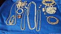 Full overview of assorted freshwater pearl jewelry on blue fabric, including necklaces, bracelets, earrings, loose beads.