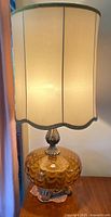 Front view of the lamp showing cream fabric shade and amber glass base with metallic accents.