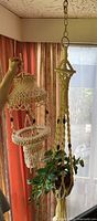 Photo showing two vintage macrame plant holders hanging side by side indoors, held up by a person to display size and detail.
