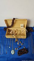 Whole lot of jewelry items including necklaces, pendants, earrings arranged on blue cloth with an open box.