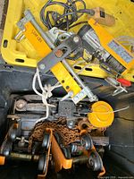 Photo showing yellow electric hoist PA100B with attached ropes and electrical cable, placed in yellow bin along with mechanical jacks and chains.