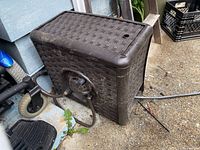 Side view of the brown Suncast hose reel box with hose partially visible and slightly dirty footprint around it.