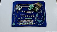 Photo shows an assortment of necklaces, bracelets, earrings on a blue velvet display. Includes turquoise and silver-tone bracelets, bead necklaces, and earrings, with one pair boxed.
