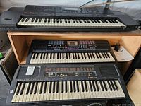 Four keyboards stacked in storage, top and middle clearly identified as Roland G600 and Yamaha Portasound PSS-480 respectively, bottom keyboard Kawai X130.