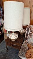 Two ceramic table lamps on wooden side table under shelves