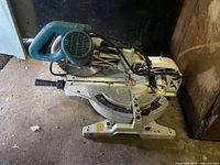 Full side view of a Makita compound miter saw with blue handle and metal stand, shows overall design and wear.