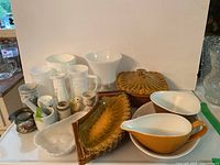 Overview of all items arranged on white surface showing milk glass vases, various cups, mid century modern ceramic snack server set, condiment dishes, gravy boat and ceramic bowl.