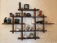 Full view of wooden wall-mounted shelf with miniature figurines made of metal, porcelain, and pottery arranged on multiple tiers.