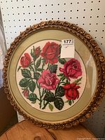Front view of round petit point needlework with rose bouquet in ornate gold-tone frame