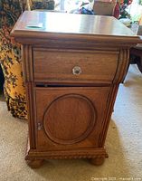 Solid wood side table front view showing drawer with glass knob and cupboard door with round raised panel design and lock.