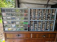 Two blue plastic organizer drawer units with multiple small transparent drawers, placed on a wooden surface. Drawers labeled and filled with components.