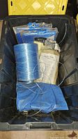 Photo showing plastic bin containing several folded blue tarps and a smaller spool of blue nylon twine along with packaging.