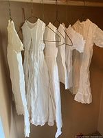 Five white baby dresses hanging on hangers, showing overall view of length and styles