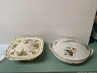 Two vintage porcelain casserole dishes side by side, one square with floral decoration and unique handles, the other oval with multicolor floral design and side handles.