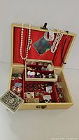 Full top view of open jewelry box showing necklaces draped over lid, multiple pairs of earrings, brooches, and jewelry parts arranged inside compartments
