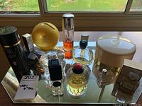View of various vintage perfume bottles and talcum powder containers on glass surface with reflection, bottles include Hermes, Tabu, Acqua, and Guilty set