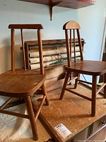Two vintage wooden chairs with spindle backs placed next to a wooden tabletop desk that has educational maps and rolled lessons mounted on it.