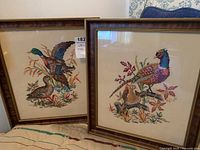 Two framed petit point wildlife bird needlework artworks shown side by side. One depicts a pheasant and chick, the other a pair of ducks.