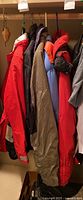 Seven vintage winter coats hanging in a row on hangers, showing a variety of colors and styles including bright red, brown, blue, and black.