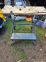 Front view of Black & Decker Workmate workbench showing wooden top with holes and worn surface, metal legs and shelf underneath.