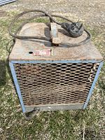 Front view of the rectangular metal garage heater showing rust and power cable with plug coiled on top.