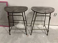 Front view of two bar stools side by side on floor showing wooden seats and tubular metal frames.