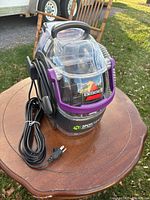 Front view of Bissell Spot Cleaner on wooden table, showing machine body, handle, and cord.