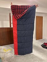 Photo showing full length of blue and red rectangular sleeping bag with buffalo plaid lining inside.