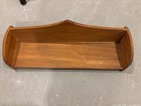 Wooden wall-mounted shelf viewed from an angle showing curved sides and pointed decorative top.